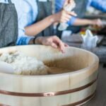 Close-up of sushi rice being prepared by chefs in a bright modern kitchen setting.