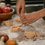 Crop anonymous female chef making homemade Italian pasta nests while cooking in modern kitchen